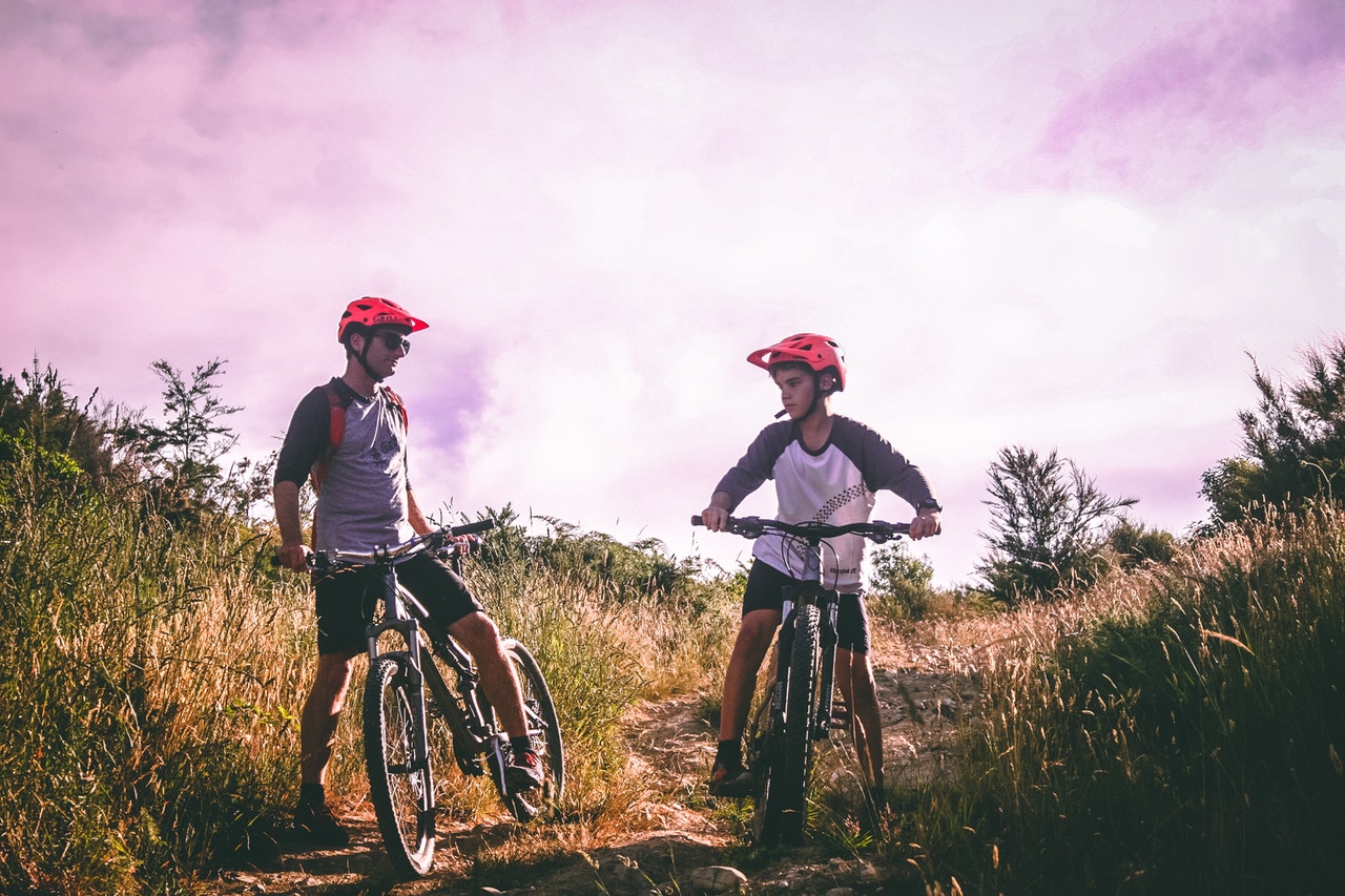 two-man-riding-mountain-bike-on-dirt-road-at-daytime